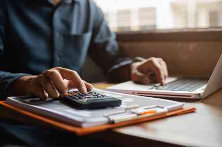 Person mit Taschenrechner und Laptop